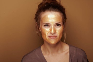 Bronz arka plan karşı altın kozmetik yüz maskesi ile modern kadın portresi.