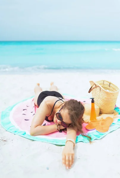 放松时尚 岁妇女戴着太阳镜 长卷发在优雅的黑色泳衣在白色海滩上睡在圆毛巾 — 图库照片