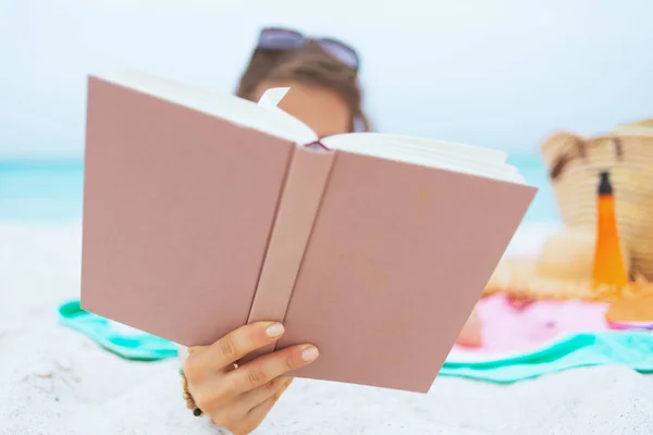 时尚中年妇女与长卷发在优雅的黑色泳衣上的白色海滩阅读书 — 图库照片