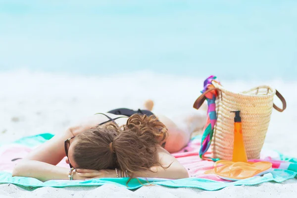 时髦的40岁女人长卷发在优雅的黑色泳衣在白色沙滩上睡觉 而日光浴 — 图库照片