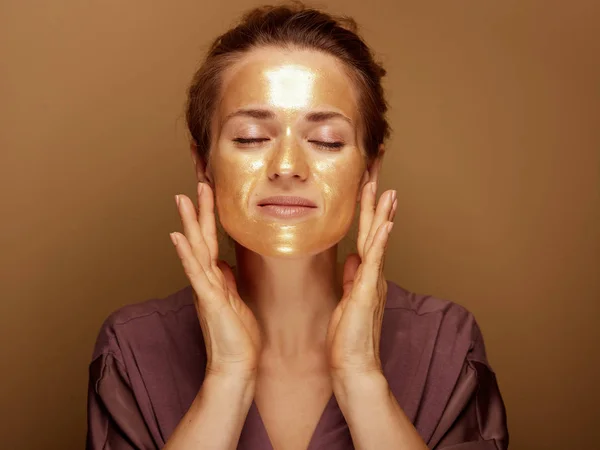 Porträtt Avslappnad Medelålders Kvinna Med Gyllene Kosmetiska Ansiktsmask Gör Ansiktsmassage — Stockfoto