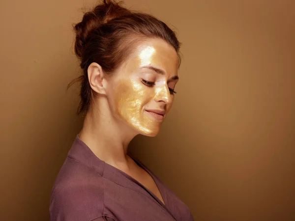 Portret Van Jonge Huisvrouw Met Gouden Cosmetische Gezichtsmasker Tegen Bronzen — Stockfoto