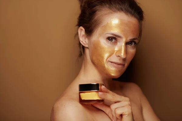 现代女性的肖像与黄金化妆面罩持有化妆品罐孤立在青铜背景 — 图库照片