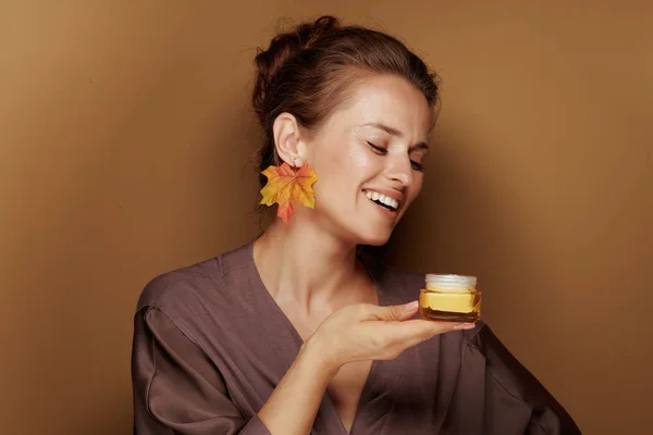 你好秋天 微笑优雅的女人在浴袍与秋叶耳环的肖像享受在棕色背景的面部Créme的香味 — 图库照片