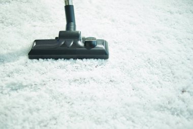 Elektrik süpürgesine yakın çekim. Beyaz kabarık halı süpürüyor..