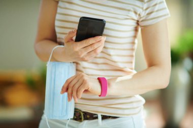 Modern orta yaşlı kadın, akıllı telefon ve spor takip cihazı ile evin günlük adımlarını kontrol ediyor. Koronavirüs karantina konseptinde ağırlık kontrolü