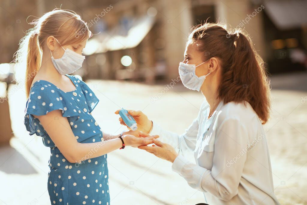 Life during coronavirus pandemic. elegant mother and child with medical mask disinfecting hands with sanitiser outdoors in the city.