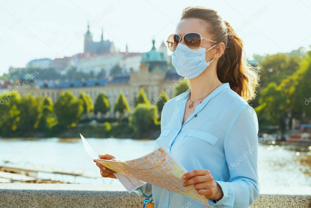 Life during coronavirus pandemic. modern traveller woman in blue blouse with medical mask, sunglasses and map looking into the distance and exploring attractions outdoors on the city street.