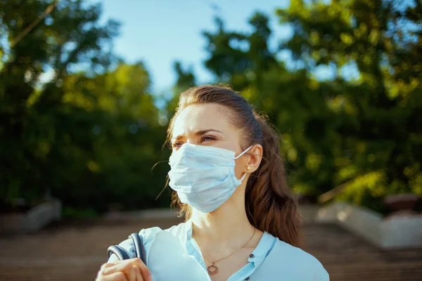 コロナウイルスのパンデミックの間の生活 青いブラウスに街の外の距離を調べる医療マスクの若い女性 — ストック写真