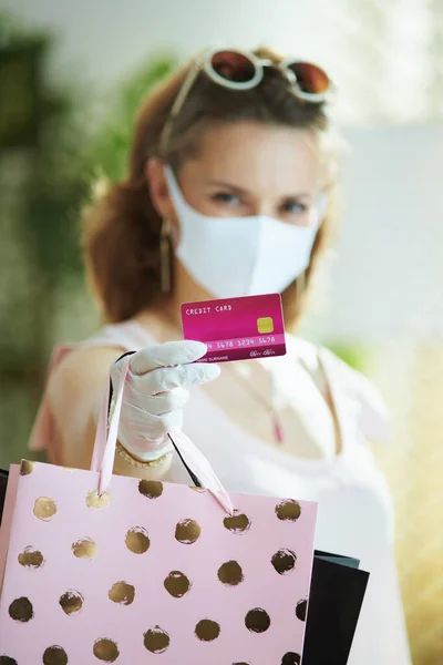 Covid 19パンデミックの間の生活 中世の女性の買い物客に閉鎖でピンクのブラウスで医療マスク ホワイトゴム手袋 クレジットカードと紙のショッピングバッグ — ストック写真