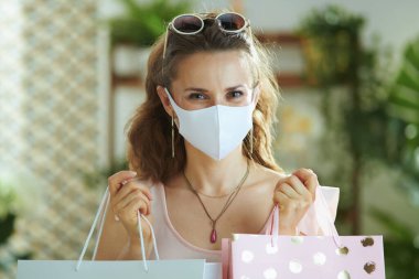 Covid-19 salgını sırasında hayat. Pembe bluzlu, tıbbi maskeli ve kağıt çantalı şık bayan alışverişçinin portresi..