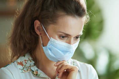 Koronavirüs salgını sırasında hayat. Tıbbi maskeli, beyaz bluzlu, düşünceli genç bir kadın..