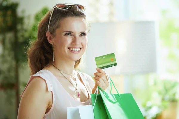 smiling modern 40 years old woman shopper in sunglasses with credit card and paper shopping bags.