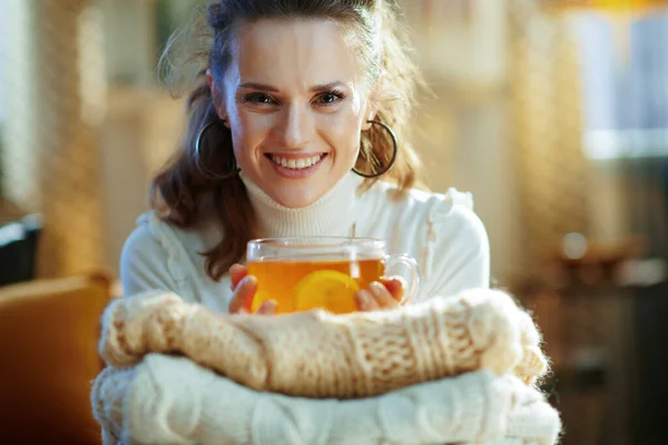在阳光明媚的冬日里 身穿白色毛衣 头戴毛衣 头戴茶杯 头戴柠檬 面带微笑的中年女性 — 图库照片