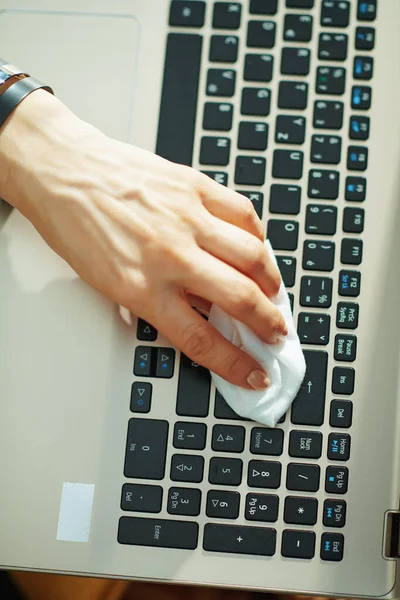 Closeup on woman cleaning laptop keyboard with cleaning cloth in the living room in sunny day.