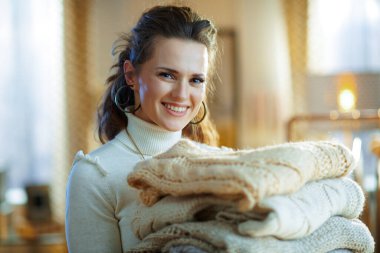 Güneşli kış gününde modern oturma odasında beyaz kazak ve etek giyen gülümseyen orta yaşlı kadın portresi..