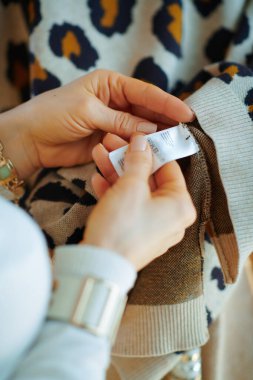 Güneşli kış gününde, modern oturma odasında beyaz kazak ve etek giyen orta yaşlı bir kadına yakın çekim..