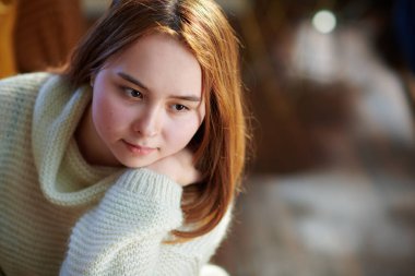 Modern evdeki güneşli kış gününde beyaz kazaklı, düşünceli genç kız portresi..