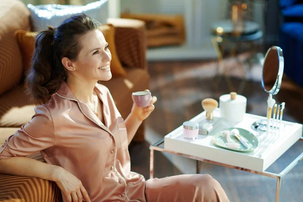 Glad Modern Kvinna Pyjamas Dricka Kaffe Nära Bord Med Toalettartiklar — Stockfoto