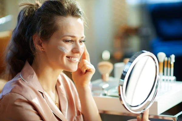 Sonriente Elegante Mujer Mediana Edad Pijama Aplicando Crema Facial Mirándose — Foto de Stock