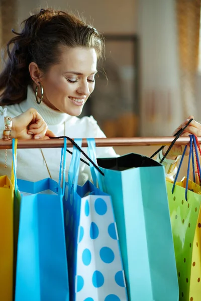 幸せな現代40歳の女性で白いセーターとスカート見てショッピングバッグハングオン銅服レール — ストック写真