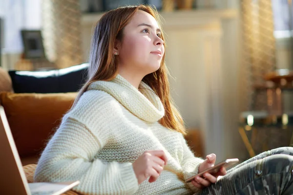 現代の10代の少女で赤い髪の白いセーターにスマートフォンを使用してアプリケーションで晴れた冬の日に現代の家 — ストック写真