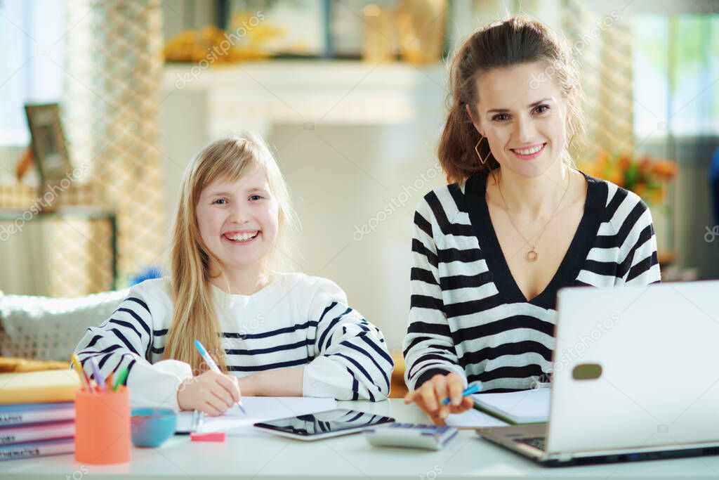 mother working while child doing homework in home office in the modern living room in sunny day.