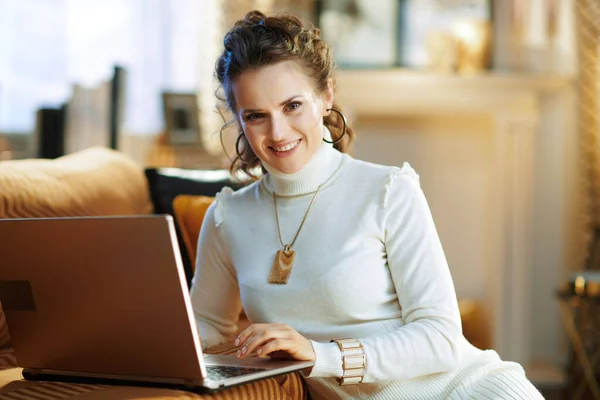 幸せな若い女性で白いセーターとスカートで現代の家で晴れた冬の日にウェブサイトを使用してノートパソコン — ストック写真