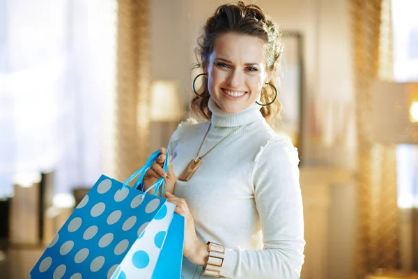 白いセーターとスカートの幸せな若い女性の肖像とともに青ショッピングバッグで現代のリビングルームで晴れた冬の日 — ストック写真