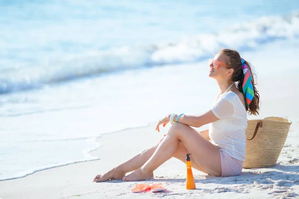 40歳のリラックスした女性に白いTシャツとピンクのショートパンツが海沿いに座って — ストック写真