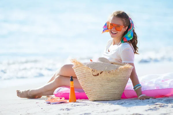 現代の笑顔40歳の女性で白いTシャツとピンクのショートパンツで海沿岸に座ってインフレータブルマットレス — ストック写真
