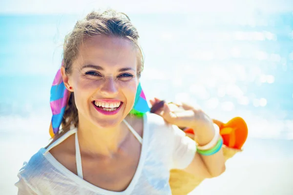 ビーチにビーチストローのバッグを持つ白いTシャツの幸せな流行の女性 — ストック写真