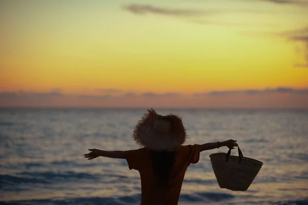 シルエットの健康的な女性とともに長いブルネットの髪でビーチバッグ喜びます上の海岸で日没 — ストック写真