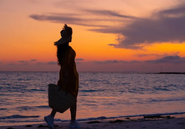 シルエットの現代女性とともに長いブルネット髪でビーチバッグ歩くとともにビーチで日没 — ストック写真