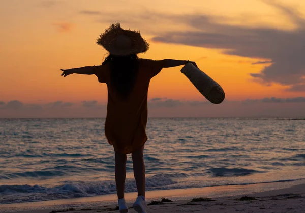 シルエットの健康的な女性とともに長いブルネットの髪を保持ビーチバッグ喜びますとともに上げ腕で海の海岸で日没 — ストック写真