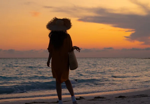 シルエットのフィット女性とともに長いブルネット髪でビーチバッグを見ながら距離に海の海岸で日没 — ストック写真