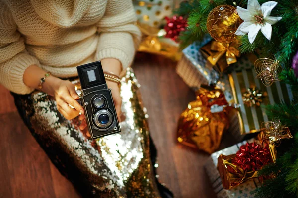 穿着金色亮片裙和白色毛衣的中年妇女在装饰过的圣诞树下 在装有复古摄影相机的礼盒附近的衣服 — 图库照片