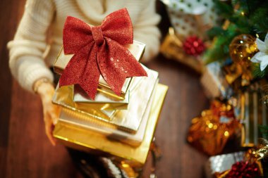 Altın pullu etekli modern ev hanımı ve Noel ağacının altında bir yığın hediye kutusu olan beyaz süveter.