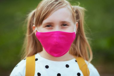 Koronavirüs salgını sırasında hayat. Beyaz benekli bluzlu, pembe maskeli, açık hava okulundan dönen modern bir kızın portresi..
