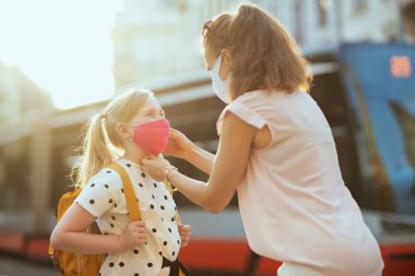 Covid-19 salgını sırasında hayat. Modern anne ve okul kızı maskeli ve sarı sırt çantalı açık hava okuluna hazırlanıyor..