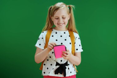 Koronavirüs salgını sırasında hayat. Sarı sırt çantalı, beyaz benekli bluzlu mutlu modern kız kara tahta yeşil arka planda izole edilmiş cep harçlıklarını sayıyor..