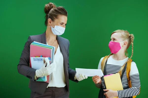 带口罩的现代女教师和女学生 海盗测试结果医疗证明和黑板绿色背景课本 — 图库照片
