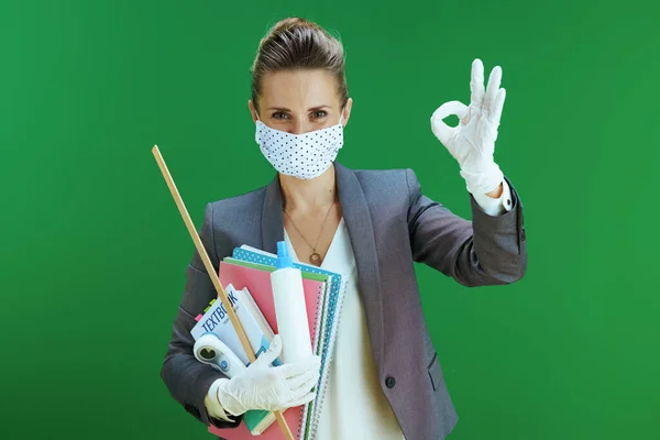 快乐的现代中年女教师 身穿白衬衫 戴着医疗面罩 橡胶手套 数字温度计 课本和卫生纸 在黑板绿色背景上摆出一副不错的姿势 — 图库照片