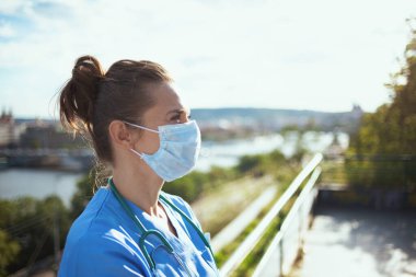 Koronavirüs salgını. Steteskop ve tıbbi maske takmış modern doktor kadın şehrin uzak köşelerine bakıyor..