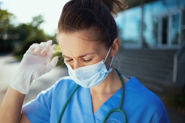 Covid-19 salgını. Steteskop ve tıbbi maskeli, üniformalı modern doktor kadın kliniğin yakınında..