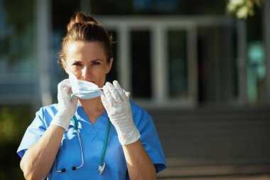 Koronavirüs salgını. Steteskop ve sağlık maskesi takmış modern doktor kadın klinik yakınlarında..