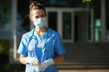 Koronavirüs salgını. Steteskoplu, tıbbi maskeli ve hastane yakınlarında kahve içen modern doktor portresi..