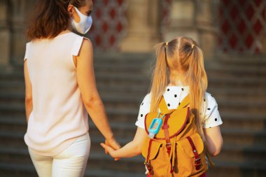 Koronavirüs salgını sırasında hayat. Modern anne ve okul öğrencisinin arkasında sarı sırt çantası ve antiseptikle okula giderken görülmüş..