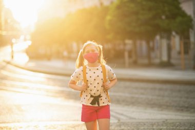 Koronavirüs salgını sırasında hayat. Beyaz benekli bluzlu, pembe maskeli ve sarı sırt çantalı modern bir öğrenci açık hava okulundan geliyor..