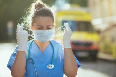 Koronavirüs salgını. Ambülansın yanında steteskop ve tıbbi maske takan modern sağlık görevlisi kadın..